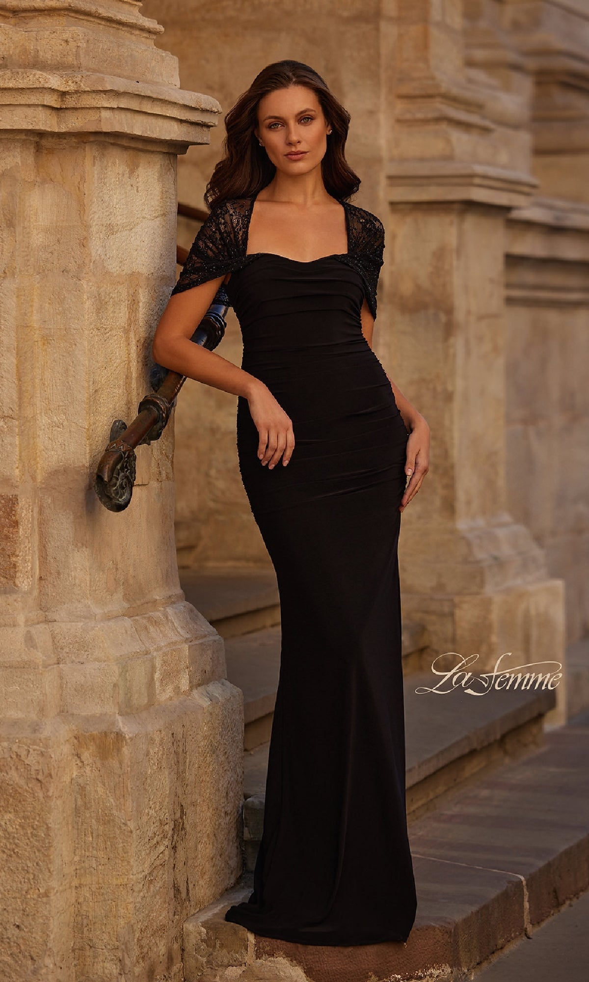 Woman in a fitted Lace-Sleeve Black Formal Dress: La Femme 33133 stands against a stone wall outdoors.